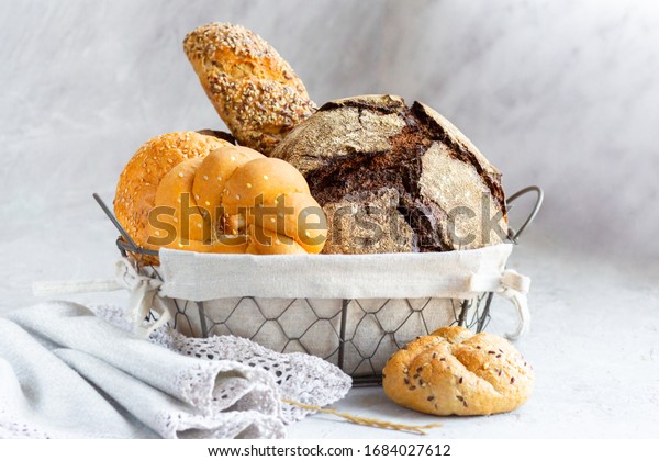 Bread in a basket with\
rolls. Fresh bakery. Beautifully folded black and white bread in a\
metal basket. Baking in a bread box. Baking bread at home. Home\
baking on the table.