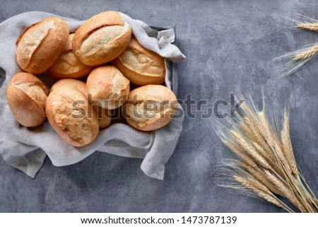 Bread buns in basket on rustic wood with wheat ears, top view on grey textured background