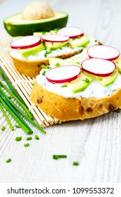 Bread with cheese spread, sliced avocado, and radishes