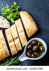 Bread Ciabatta, Arugula, Olives, Rosemary On Stone Slate Black Background. Top View