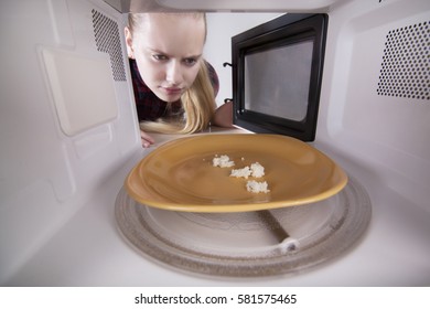 Bread Crumbs On Plate In Microwave. Girl Opened The Door Looking Inside The Oven. The Studio On White Background