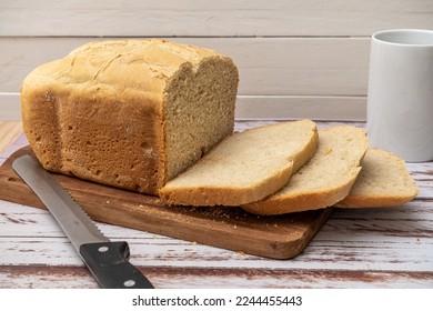 A bread last made with a home bread machine with freshly cut slices on a wooden board next to the bread knife and a cup. - Powered by Shutterstock