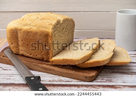 A bread last made with a home bread machine with freshly cut slices on a wooden board next to the bread knife and a cup.