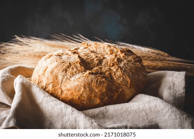 A Bread Loaf On A Cotton Rag With Wheat Spikes, Black Background, And Copy Space