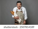 Bread seller, baguette in bakery on gray background. Mature french baker holding baguette in hands.