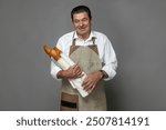 Bread seller, baguette in bakery on gray background. Mature french baker holding baguette in hands.