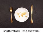 Bread in shape world map on white plate. Gold fork and knife on a dark stone background. Abstract Concept of global hunger.