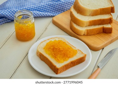 Bread slice with orange marmalade jam on white plate