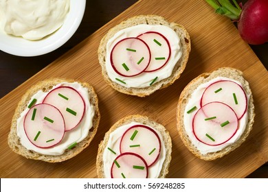 Bread Slices With Cream Cheese, Radish Slices And Chives On Wooden Board, Photographed Overhead With Natural Light (Selective Focus, Focus On The Top Of The Canapes)