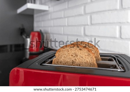 Bread slices inside red kitchen toaster on black countertop in modern home kitchen interior