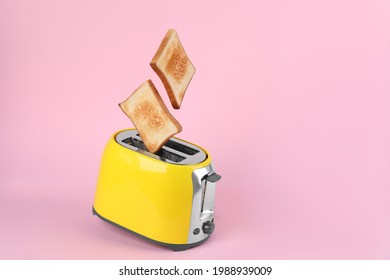 Bread slices popping up from modern toaster on pink background. Space for text