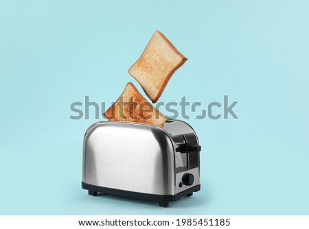Bread slices popping up from modern toaster on light blue background