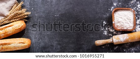 bread with wheat ears and bowl of flour on dark board, top view