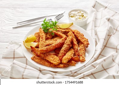 Breaded And Baked Fish Sticks, Fish Fillet Fingers Served On A White Plate On A Wooden Table With Tartar Sauce And Lemon Wedges, Landscape View From Above