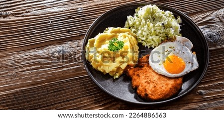 Breaded chicken cutlet served with fried chicken egg, potatoes and cabbage