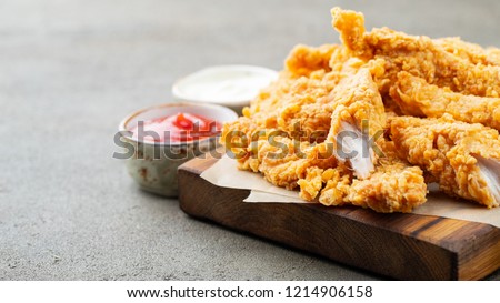 Breaded chicken strips with two kinds of sauces and fried potatoes on a wooden Board. Fast food on dark brown background. with copy space