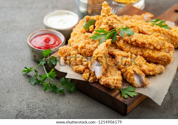 Breaded chicken strips with\
two kinds of sauces on a wooden Board. Fast food on dark brown\
background