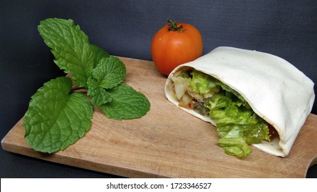 Breaded Chicken In A Tortilla Wrap With Lettuce And Tomato, With Mint Leave And Tomato As Properties. Isolated On Black Background