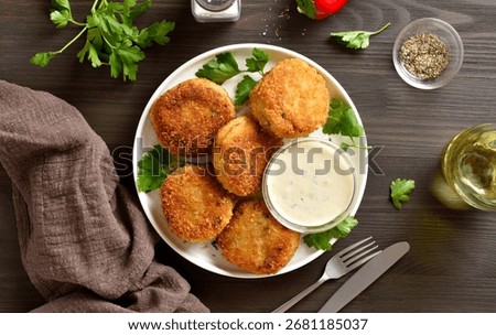 Breaded fish cakes from mashed potato and minced fish served with dipping sauce on white plate on brown wooden table. Top view, flat lay