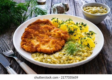 Breaded fried pork chop with bone, boiled potatoes and boiled cabbage on wooden table 