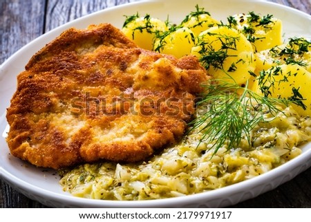 Breaded fried pork chop with bone, boiled potatoes and boiled cabbage on wooden table 