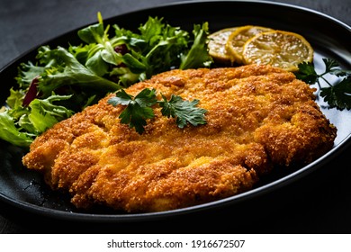 Breaded fried pork chop and fresh vegetables on black table 