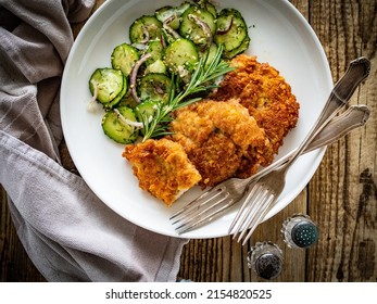 Breaded Fried Pork Chop With Sliced Cucumbers And Rosemary On Wooden Table 