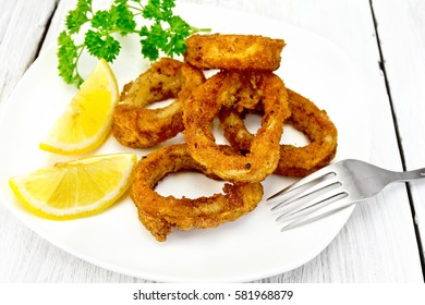 Breaded fried squid rings on a plate with slices of lemon and parsley on the background light wooden boards