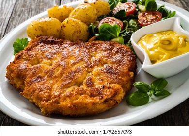 Breaded pork chop with boiled potatoes and vegetable salad on wooden background
