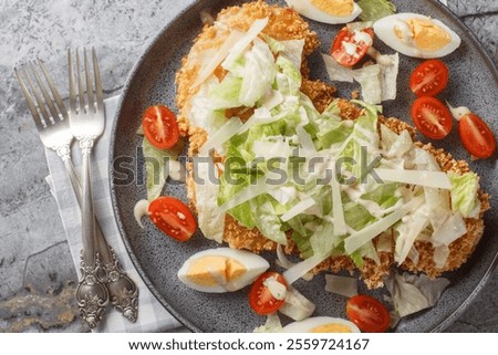 Breaded schnitzel Caesar salad with crispy chicken meat, eggs, parmesan, iceberg lettuce and tomatoes close-up in a plate on the table. horizontal top view from above