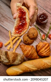 Breads. Buns With Jam. Hand Holding Slice Of Bread With Jam And Other Buns Blurred In The Background.