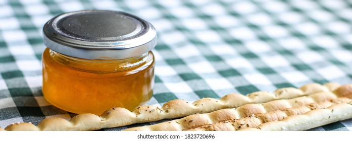 Breadsticks or Italian grissini snack with jar of honey on green gingham tablecloth. Food, harvest concept. Banner.