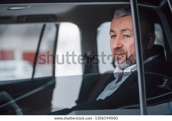 Break between trip. Senior businessman in\
official clothes sitting in a modern new\
car.