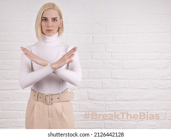 Break the bias symbol of woman's international day. The arms of a girl in white are crossed on a white brick wall. Woman arms crossed to show solidarity, breaking stereotypes, inequality
