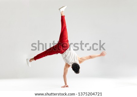 Break dancer doing handstand stunt on one hand and splitted out legs over white studio background