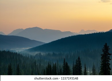 Break of dawn showing golden sunrise at Banff National Park with silhouette of distant mountain ridges and pine trees in the foreground - Powered by Shutterstock