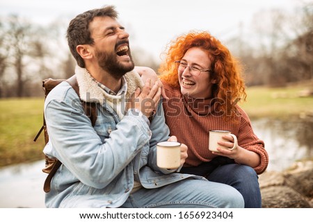 Break during a walk on a spring morning. young couple pausing warm coffee sitting on an old tree in the woods