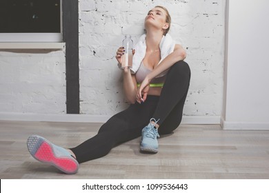 Break At Last. Full Length Portrait Of Sweaty And Tired Athletic Woman Leaning On Wall And Having Rest After Intensive Working Out. She Is Relaxing With Bottle Of Cool Drink 