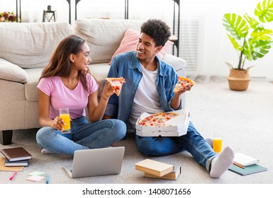 Break In Studying. Black Teen Couple Eating Pizza, Sitting On Floor With Books And Laptop At Home