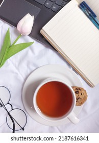 Break time concept. A cup of tea. Completed with laptop, blank book,blue pen, glasses, tulip flower and white plate.