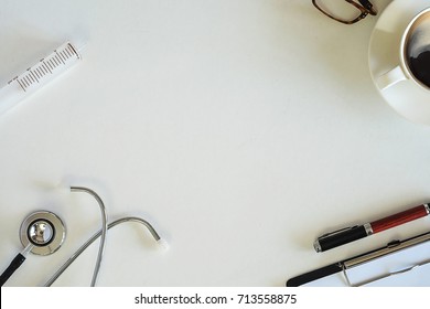 Break Time In Medical Office With White Background And Decorated By A Cup Of Coffee, Stethoscope, Glasses, Syringe, Clipboard Chart And Pen, Mock Up, Top View, Closed Up.