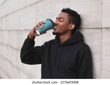 Break time! smiling young african man drinking coffee wearing black hoodie on city street over gray wall background - Powered by Shutterstock