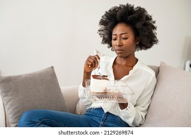 Breakdown Of Diet, Cheat Meal And Unbalanced Diet Concept. A Beautiful Young Black Woman With A Plate Of Sweets Eats Unhealthy Food At Home. An African American Lady Is Eating A Piece Of Cake