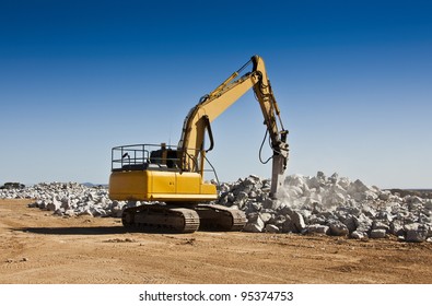 The Breaker Used To Break Up Boulders In An Open Cast Mine. Large Yellow Machinery Crushing Spodumene Ore In A Lithium Mine.