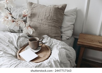 Breakfast in bed concept. Cup of coffee on wooden tray. Blank greeting card, invitation mockup. Bedroom view. Blurred beige linen pillows, blanket. Blooming magnolia branches in vase, top view. - Powered by Shutterstock