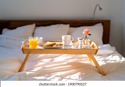 Breakfast in bed on tray at sunny morning at home - orange juice, coffee, toasts, flower. Happy Mother's day. 
