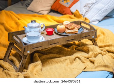 Breakfast in bed tray with waffles, apples, jam and teapot on a yellow cozy blanket with pillows. - Powered by Shutterstock