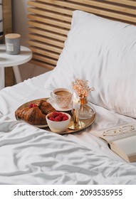 Breakfast In Bed With White Bambus Bedding. There Is A Gold Serving Tray With A Cup Of Coffee, Candle, Raspberries And Croissants.