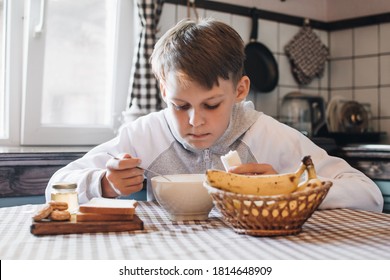 Breakfast before school in the kitchen. The boy is enjoying his breakfast.  Oatmeal and bananas for the breakfast. 