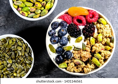 Breakfast Bowl Of Cereals Yogurt And Fruit, With Granola Oat Clusters, Blueberries, Blackberries, Apricot, Pistachio Nuts, Raspberries Oat Clusters In A Bowl, On A Black Slate Kitchen Tile